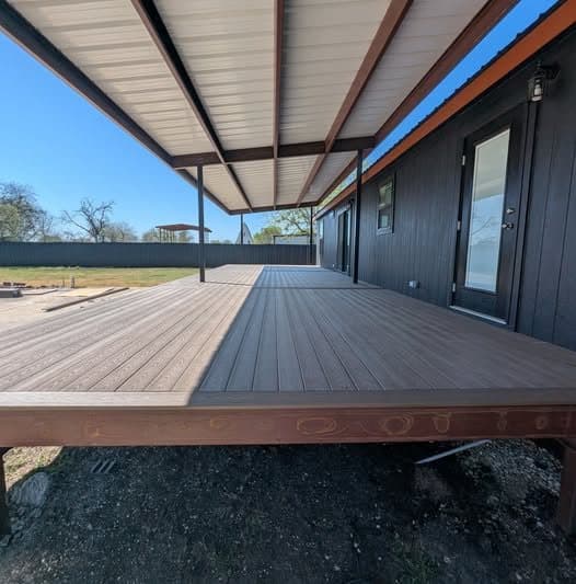 Finished covered deck with wood-tone decking under a metal patio cover beside a dark house