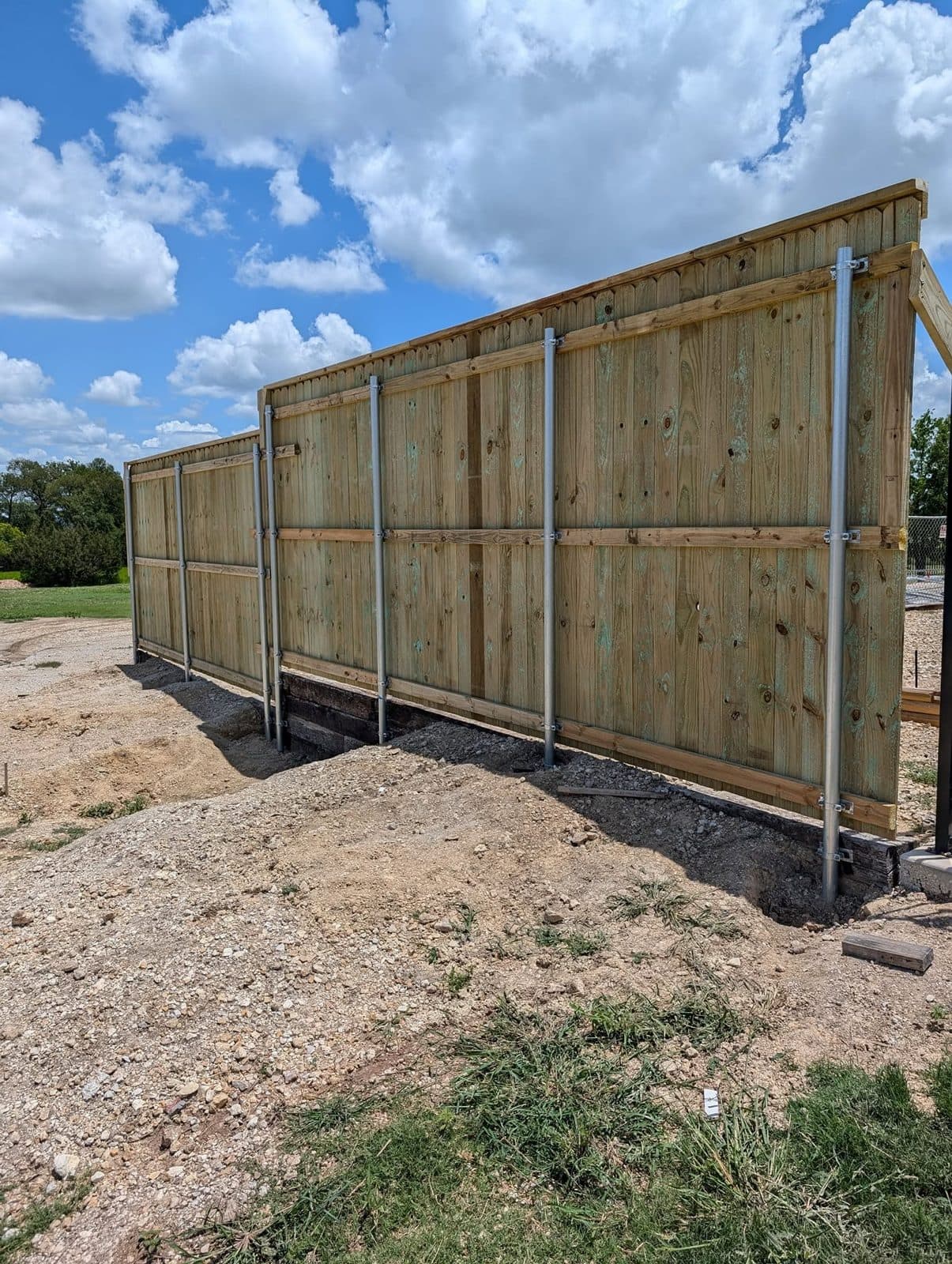 Galvanized steel posts and rails on the back of the fence, set along a railroad-tie wall