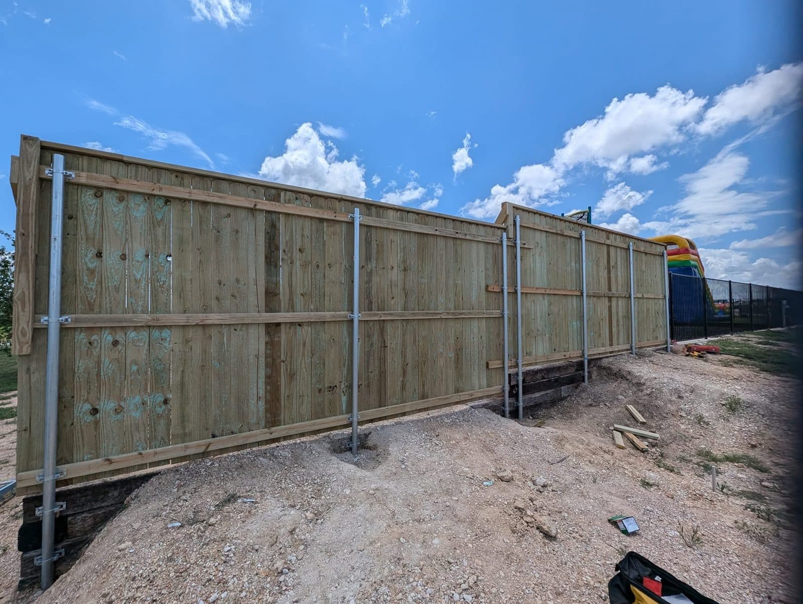 Back of the fence: three rows of wood rails clamped to galvanized steel posts, stepping along a timber wall