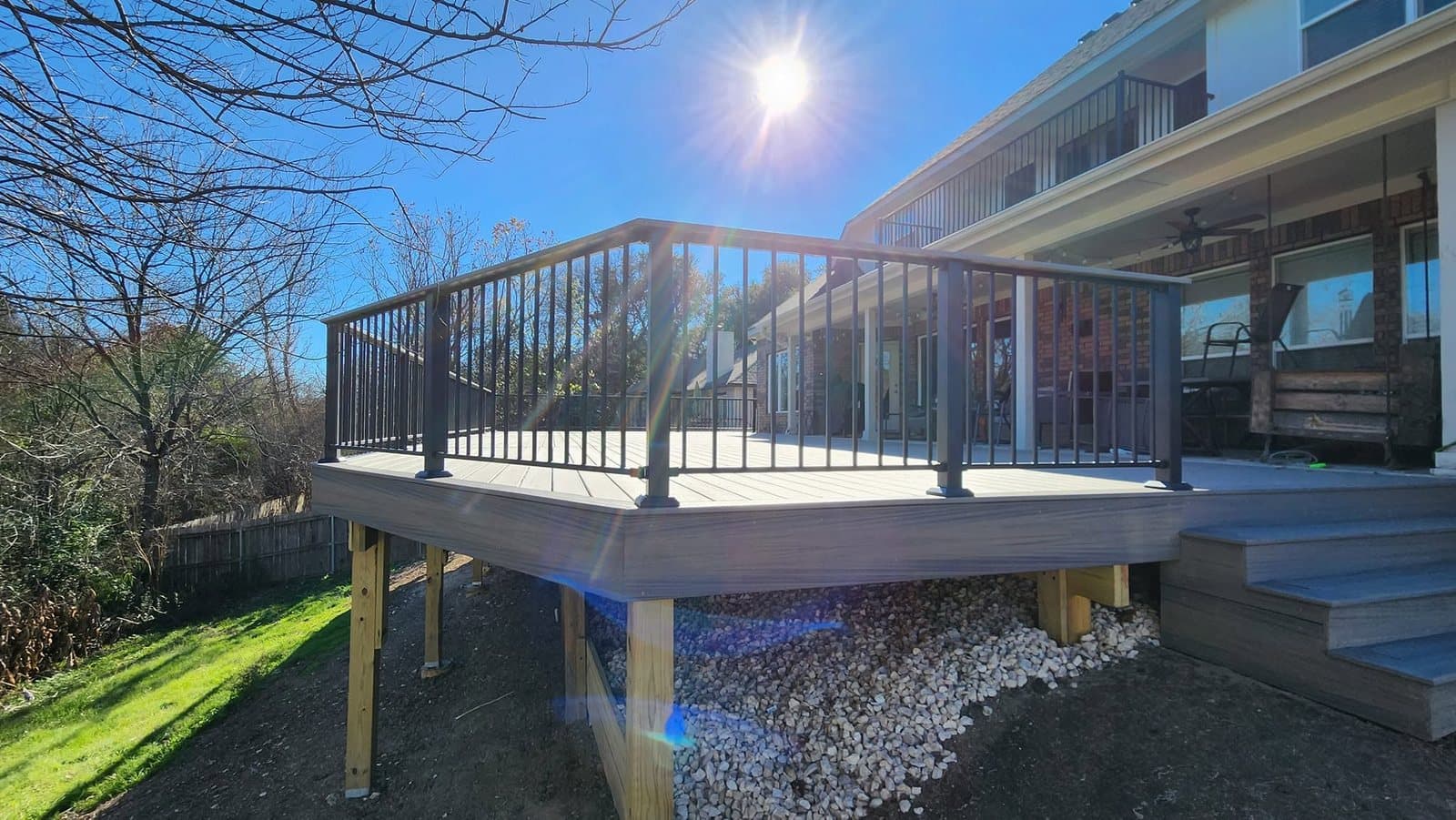 Finished raised composite deck with black metal railings and stairs off the back of a brick home