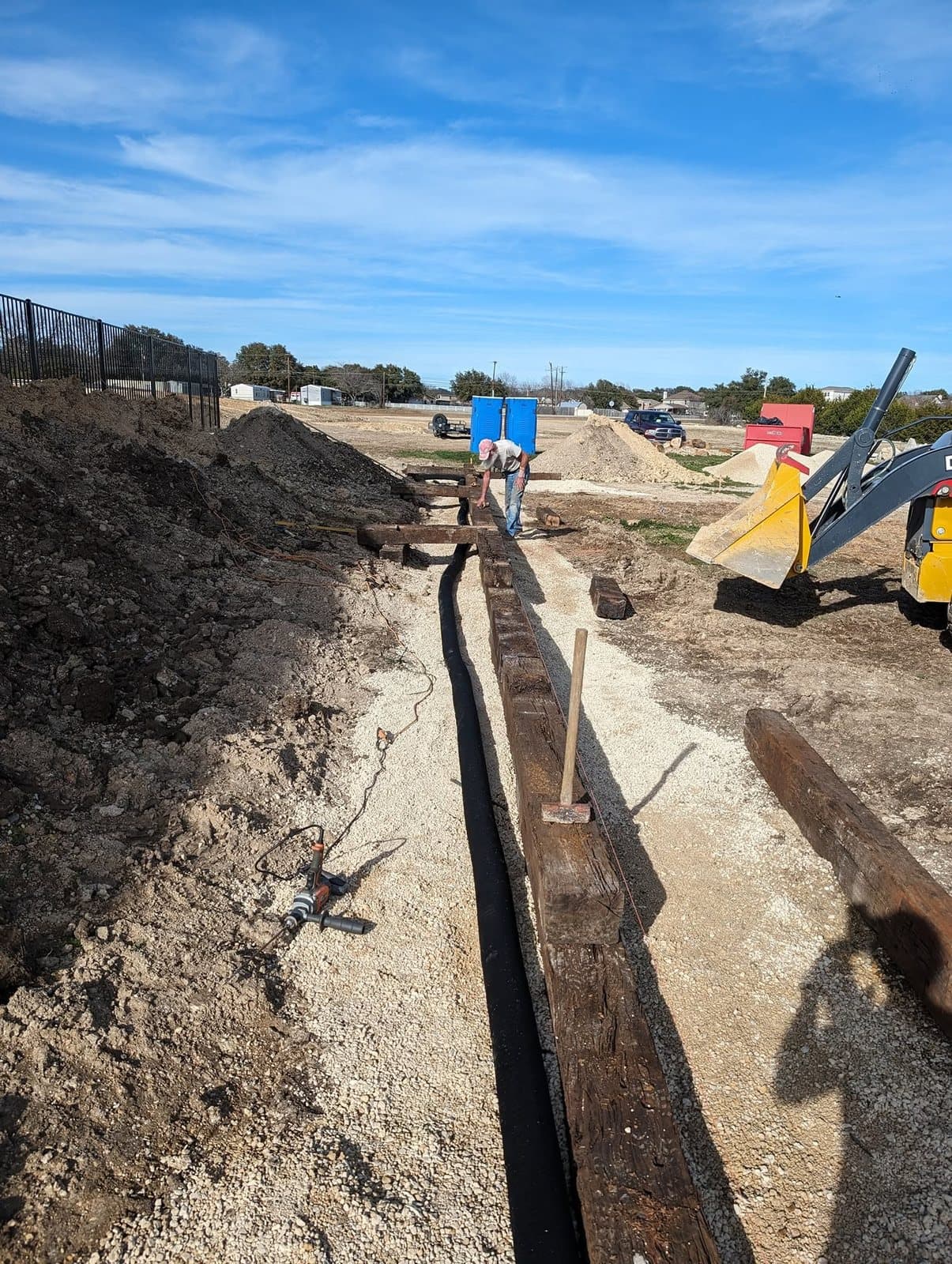 Crew member setting and leveling landscape timbers along a string line, with drain pipe laid beside them