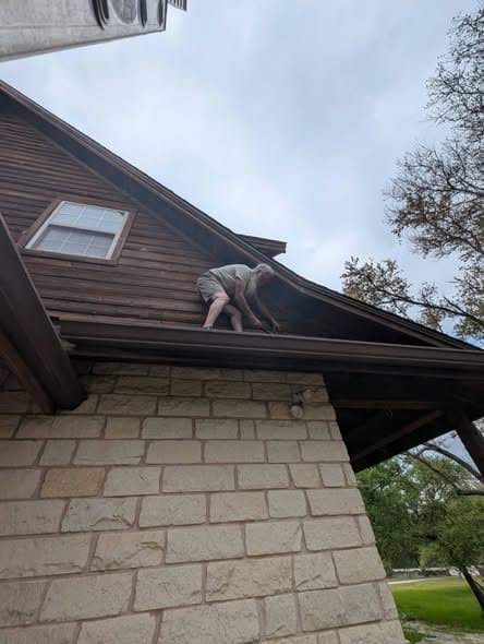 Working along the eave of a stone and wood-sided home