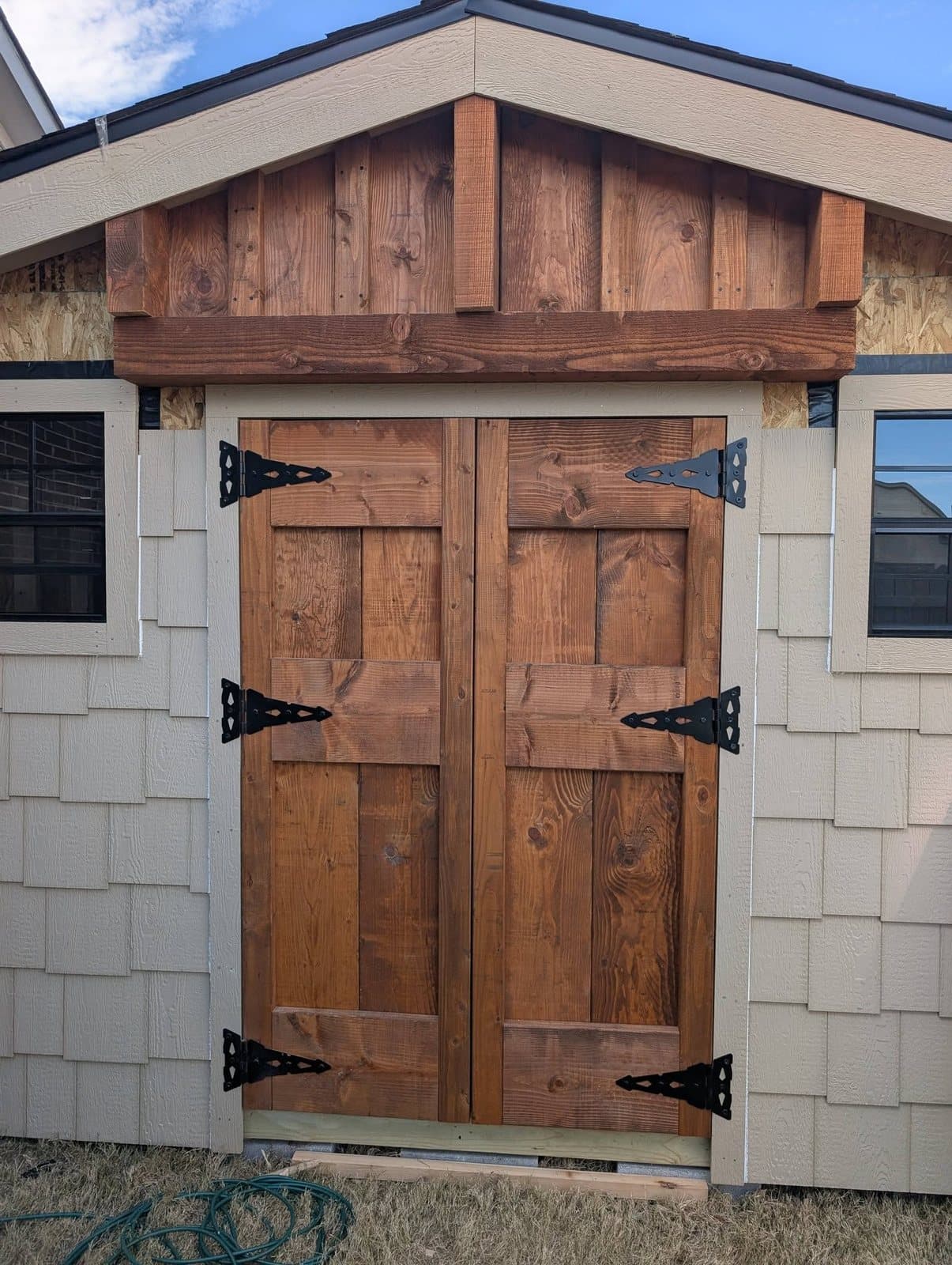 Stained cedar double doors with black strap hinges and a timber gable on a new shed